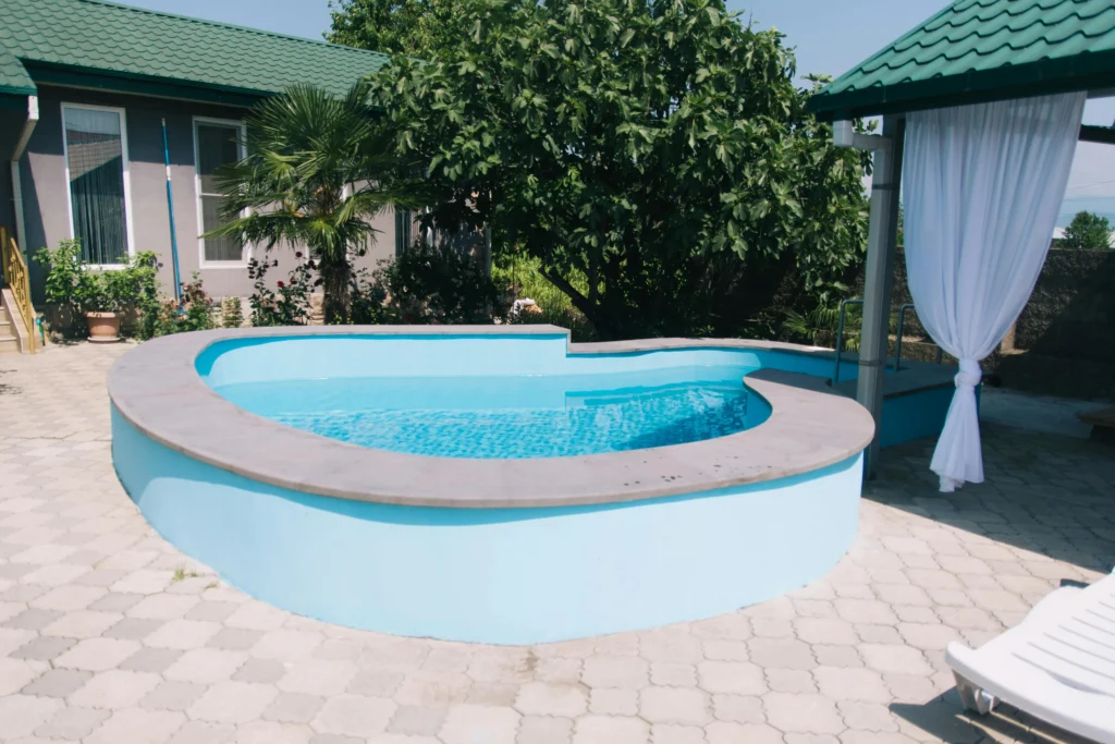 Curved outdoor swimming pool beside a garden patio with lush trees and a shaded seating area