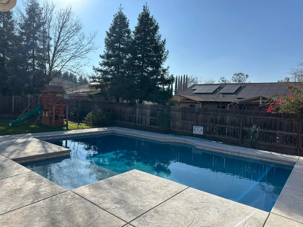 Custom residential swimming pool featuring a spacious patio and landscaped backyard design.