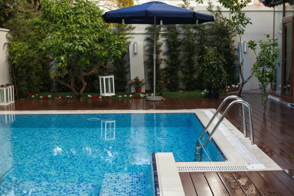 Modern outdoor swimming pool with wooden deck, garden landscaping, and pool ladder.